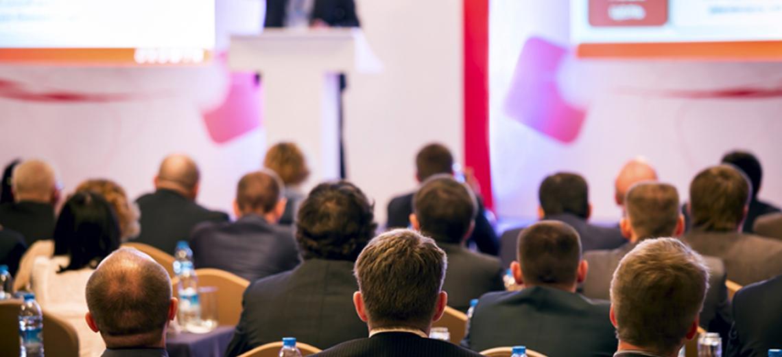 conference - a group of people facing a speaker at a podium